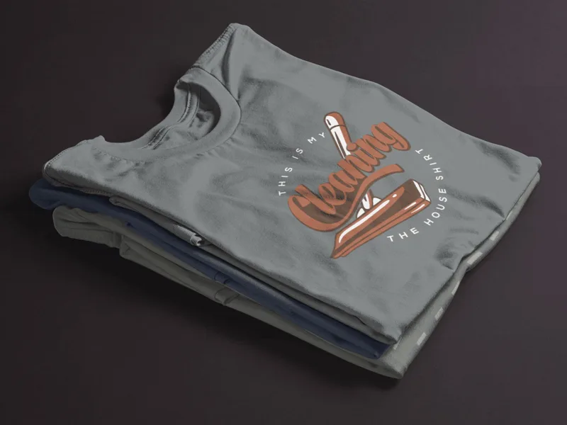 Stack of grey t-shirts with a brown graphic reading This is my cleaning the house shirt