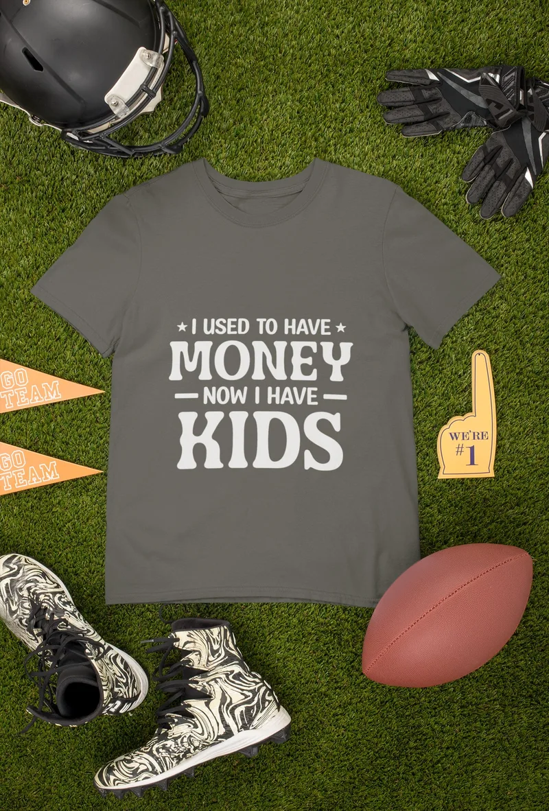 Dark grey t-shirt with I USED TO HAVE MONEY NOW I HAVE KIDS printed in white, laid out with football gear