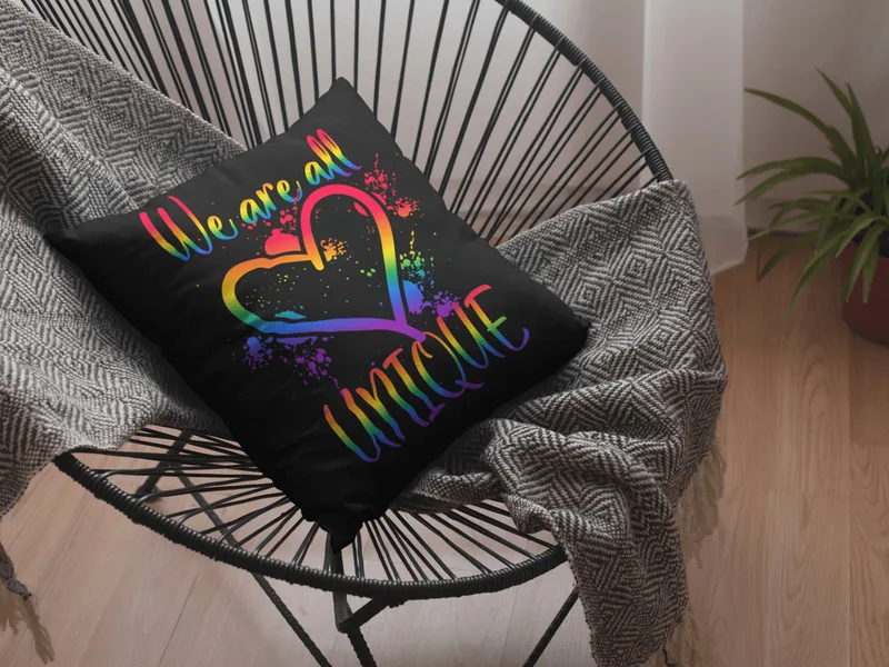 Black throw pillow with a rainbow heart and the text We are all unique