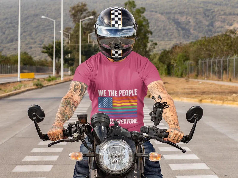 Pink t-shirt reading WE THE PEOPLE IS EVERYONE with a rainbow flag design, worn on a motorcycle