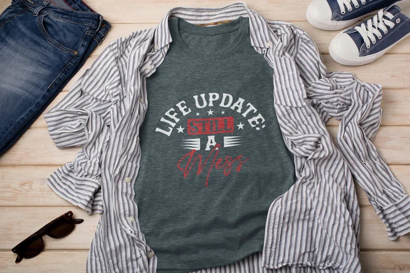 Dark grey t-shirt with Life Update Still a Mess in a red box surrounded by white stars